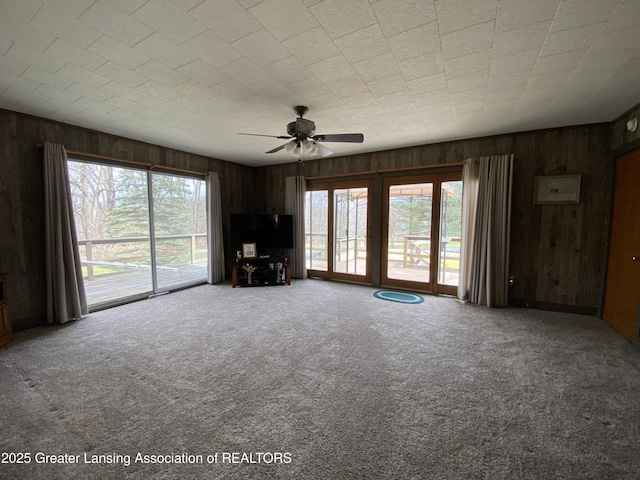 unfurnished living room featuring wood walls, a ceiling fan, carpet, and plenty of natural light