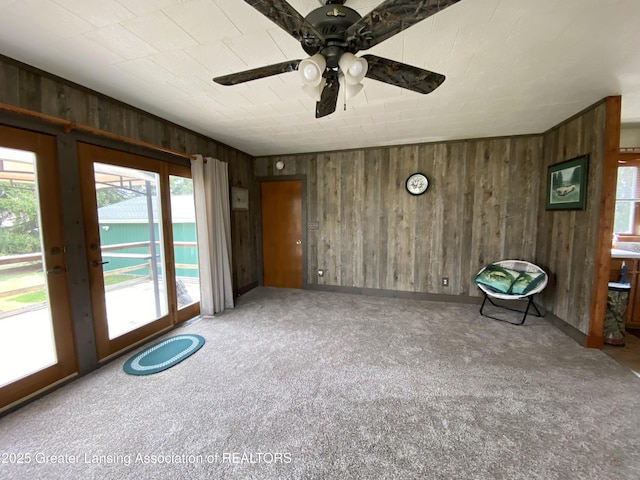 interior space with wood walls, ceiling fan, carpet flooring, and a wealth of natural light