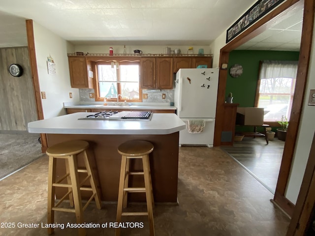 kitchen featuring brown cabinetry, tile patterned floors, freestanding refrigerator, and plenty of natural light