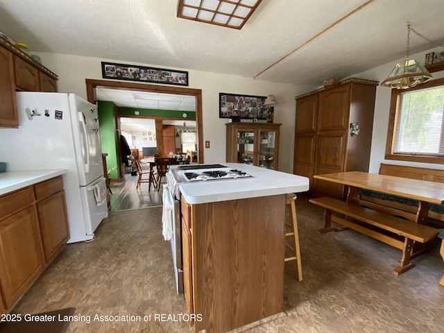 kitchen with a kitchen breakfast bar, a center island, light countertops, freestanding refrigerator, and brown cabinets