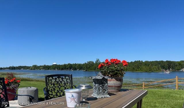 view of dock with a water view, fence, and a lawn