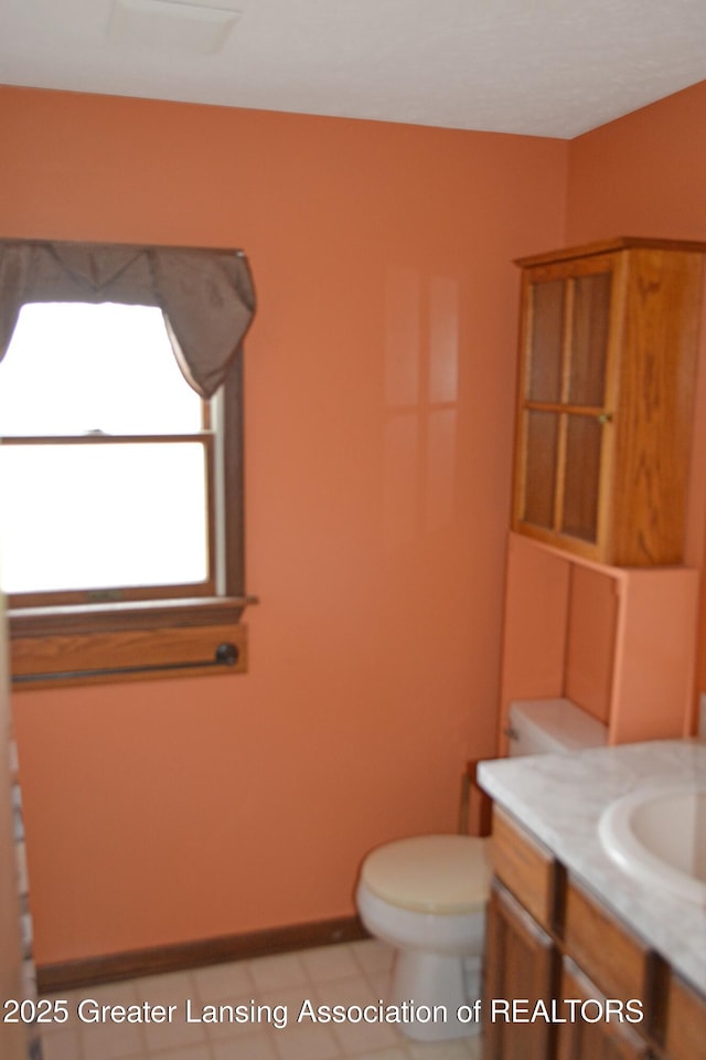 half bath featuring tile patterned flooring, toilet, vanity, and baseboards