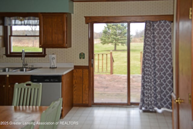 kitchen featuring wallpapered walls, light countertops, wainscoting, stainless steel dishwasher, and a sink