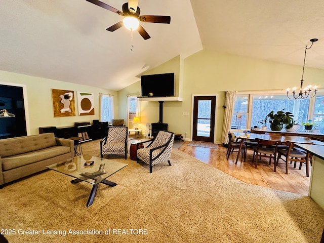 living area featuring ceiling fan with notable chandelier, a wood stove, high vaulted ceiling, wood finished floors, and baseboards
