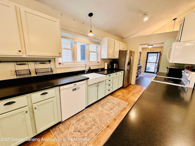 kitchen featuring light wood finished floors, a sink, white appliances, and dark countertops