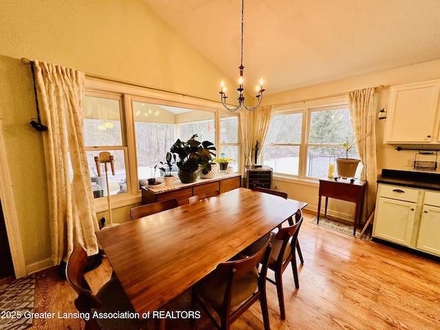 dining room featuring baseboards, light wood finished floors, a chandelier, and vaulted ceiling