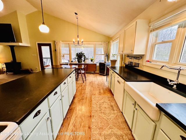 kitchen featuring decorative light fixtures, a wood stove, light wood-type flooring, dark countertops, and vaulted ceiling
