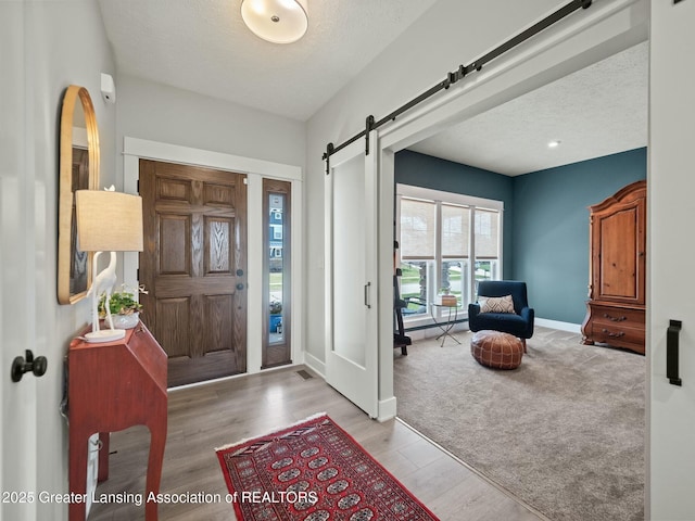 entrance foyer with a barn door, a textured ceiling, light wood finished floors, and baseboards