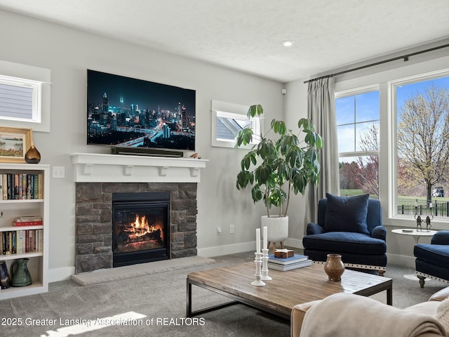 living area with baseboards, a stone fireplace, and carpet