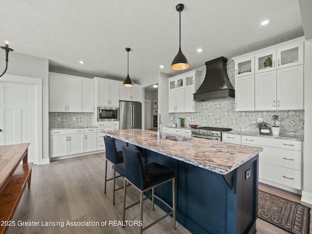 kitchen with high end appliances, white cabinets, a sink, and custom range hood