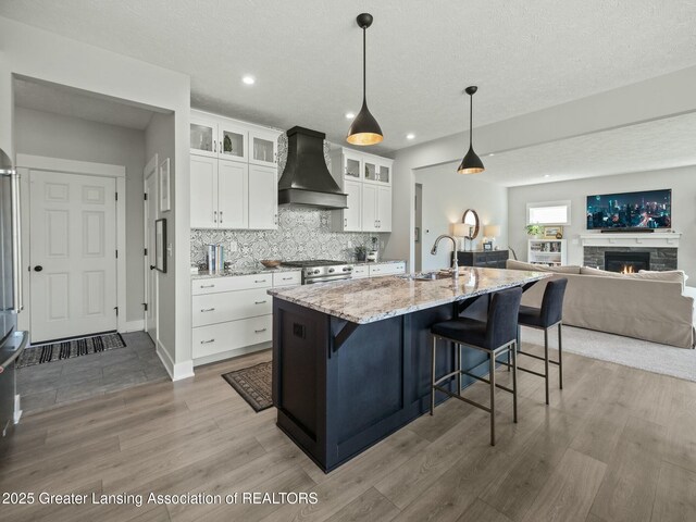 kitchen featuring high end stainless steel range, a sink, light wood-style floors, light stone counters, and premium range hood