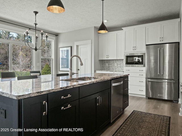kitchen with white cabinets, a sink, a textured ceiling, a center island with sink, and appliances with stainless steel finishes