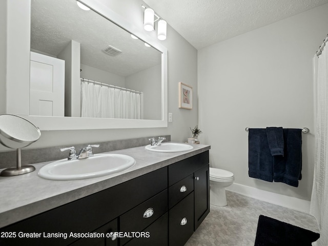 full bathroom with double vanity, a textured ceiling, toilet, and a sink