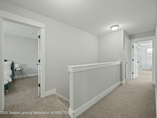 hallway featuring a textured ceiling, baseboards, carpet, and an upstairs landing