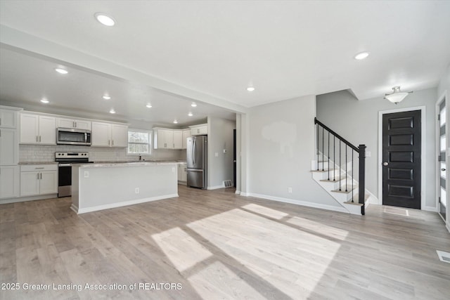kitchen featuring white cabinets, stainless steel appliances, light countertops, light wood-style floors, and open floor plan