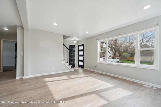 unfurnished living room featuring light wood-style floors, baseboards, visible vents, and stairs
