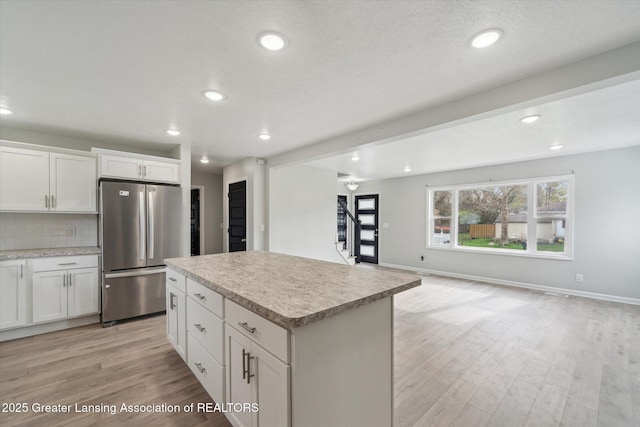 kitchen featuring light wood-style flooring, freestanding refrigerator, decorative backsplash, light countertops, and a kitchen island