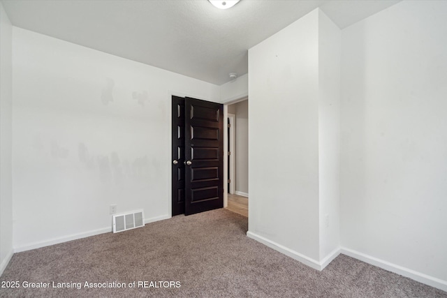 empty room with carpet floors, visible vents, and baseboards