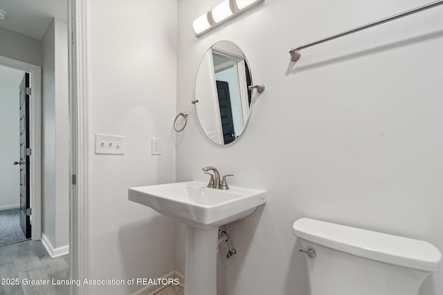 bathroom featuring wood finished floors, toilet, baseboards, and a sink