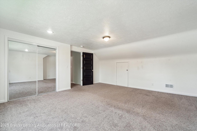 unfurnished bedroom featuring vaulted ceiling, a textured ceiling, baseboards, carpet flooring, and visible vents