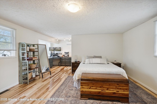 bedroom featuring a textured ceiling, baseboards, visible vents, and light wood-type flooring