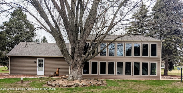 rear view of house featuring roof with shingles and a lawn