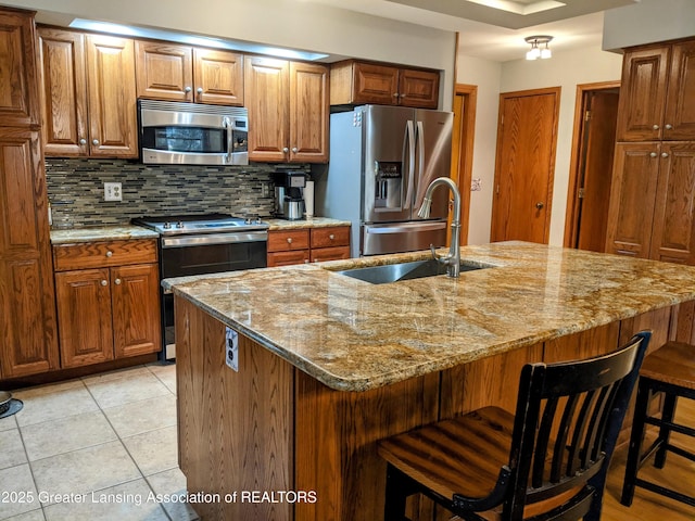 kitchen with a sink, backsplash, light stone countertops, and stainless steel appliances
