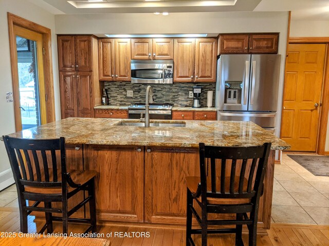 kitchen with a sink, decorative backsplash, light stone counters, and stainless steel appliances