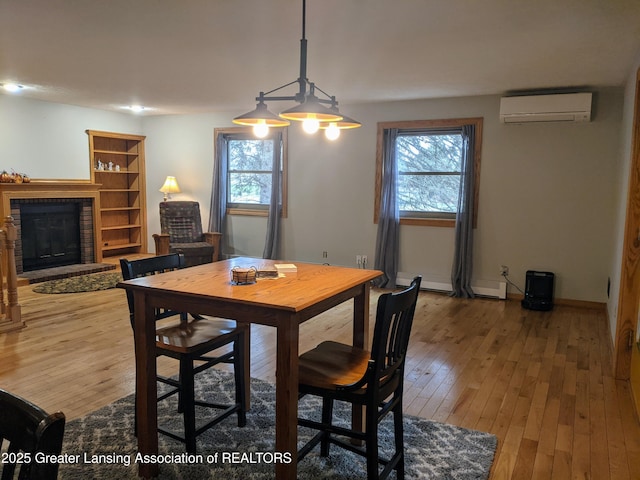 dining area featuring hardwood / wood-style floors, a wall unit AC, a fireplace, and plenty of natural light