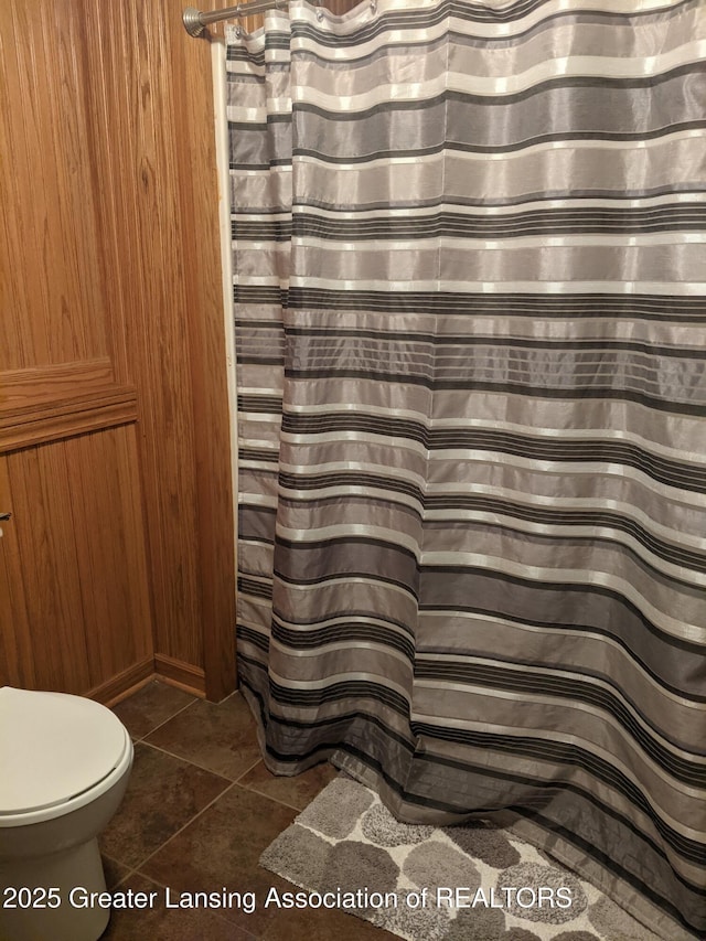 bathroom featuring toilet, tile patterned floors, a shower with curtain, and wooden walls