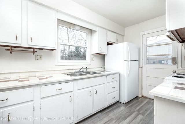 5026 Delray Dr, Lansing, MI 48910 - kitchen with tile counters, white cabinetry, freestanding refrigerator, light wood-style floors, and a sink