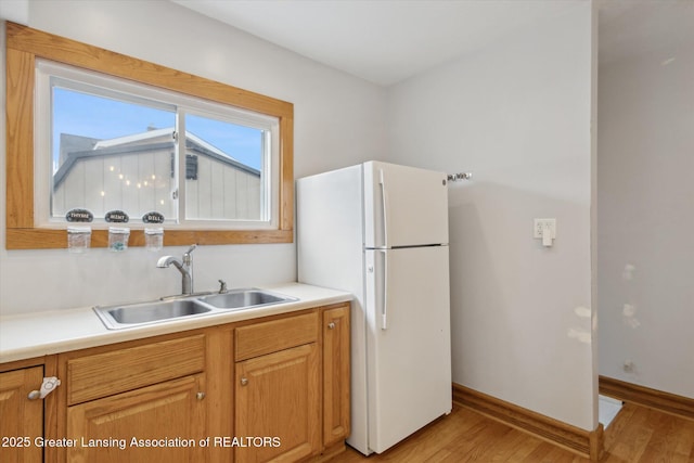 kitchen with baseboards, a sink, light countertops, freestanding refrigerator, and light wood-style floors