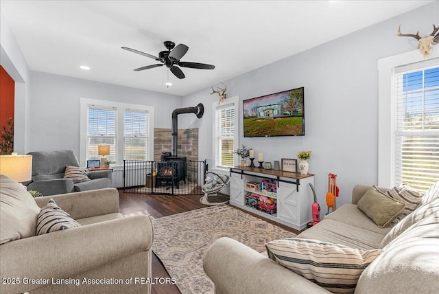 living room featuring wood finished floors, ceiling fan, plenty of natural light, and a wood stove