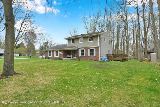 rear view of house with a deck, a yard, and brick siding