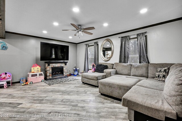 living room featuring recessed lighting, wood finished floors, ceiling fan, a stone fireplace, and crown molding