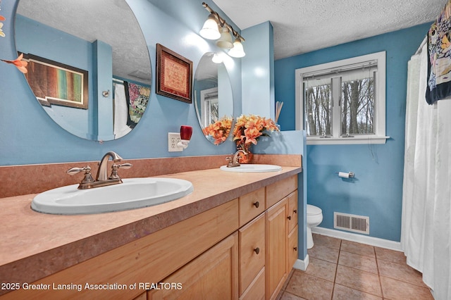 bathroom featuring a textured ceiling, a sink, double vanity, and visible vents