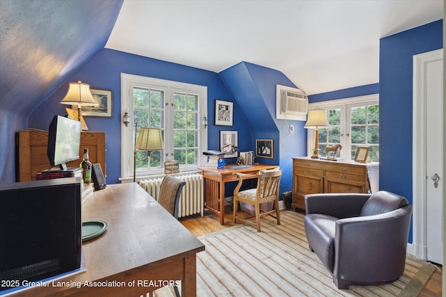 728 Audubon Rd, East Lansing, MI 48823 - home office featuring vaulted ceiling, a wall unit AC, radiator heating unit, wood finished floors, and healthy amount of natural light
