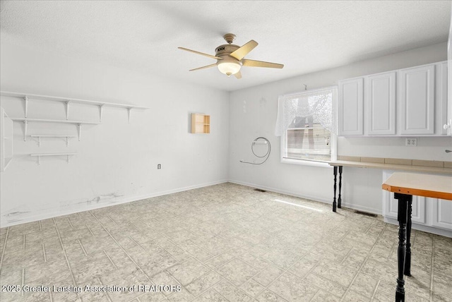 interior space featuring visible vents, baseboards, a textured ceiling, and ceiling fan