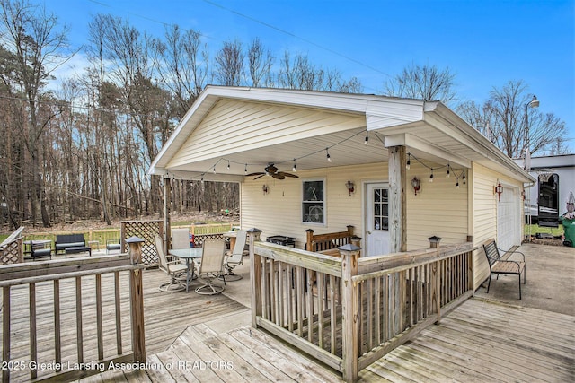 wooden terrace with outdoor dining space, a garage, and a ceiling fan