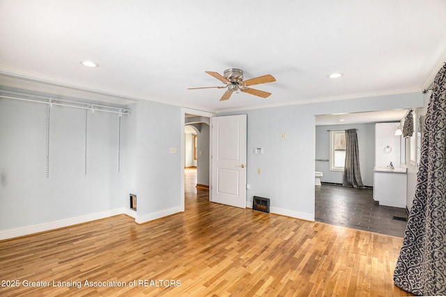unfurnished living room featuring baseboards, ornamental molding, ceiling fan, arched walkways, and wood finished floors