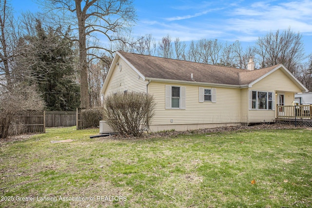 view of side of property featuring a shingled roof, a wooden deck, fence, and a lawn
