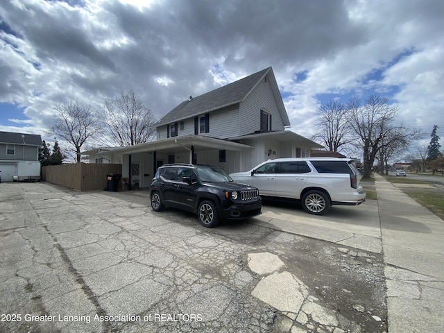 view of side of property featuring fence, an attached carport, roof with shingles, and concrete driveway