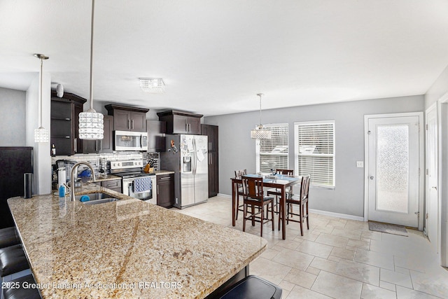 kitchen featuring backsplash, a sink, light stone countertops, dark brown cabinetry, and appliances with stainless steel finishes