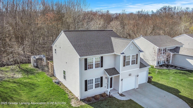 traditional-style home with concrete driveway, a view of trees, an attached garage, a shingled roof, and a front yard