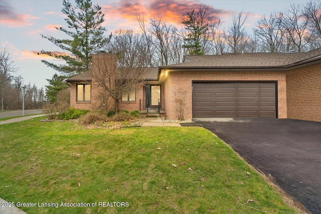 view of front of home with a chimney, aphalt driveway, a front lawn, brick siding, and a garage