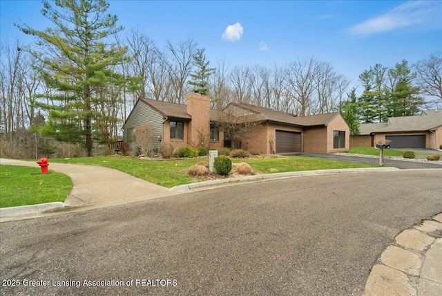 view of front of home with driveway, a chimney, a garage, brick siding, and a front yard