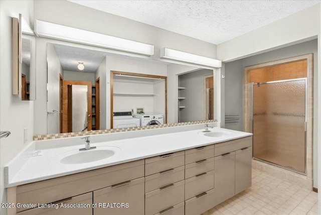bathroom with washing machine and dryer, a textured ceiling, a stall shower, and a sink