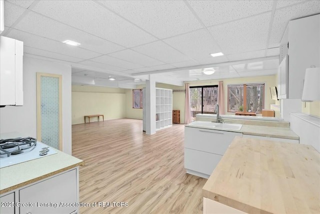 kitchen with white cabinets, a drop ceiling, a sink, white gas stovetop, and light wood-type flooring