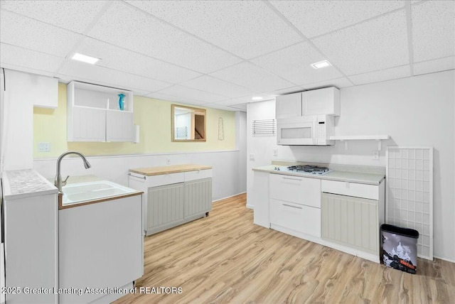 kitchen featuring light wood finished floors, a drop ceiling, a sink, and white appliances
