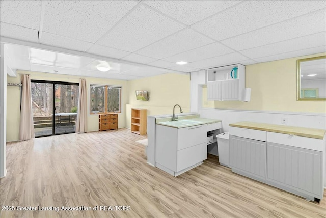 kitchen with open shelves, a sink, a paneled ceiling, and light wood-style flooring